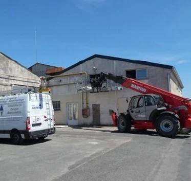 Engin de chantier et camionnette devant un bâtiment pendant les travaux de rénovation